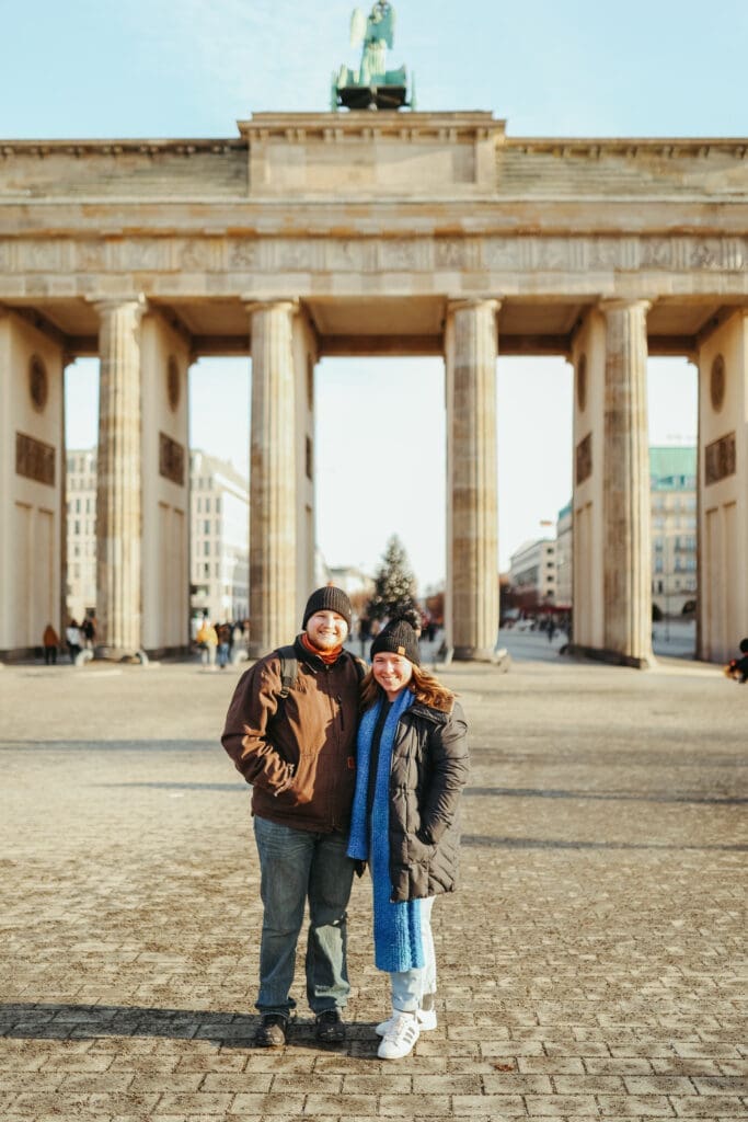 a husband and wife dressed in winter clothes standing in front of the berlin gate